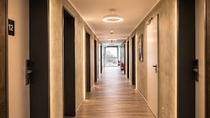 A hotel corridor with wooden flooring, dark doors, and a view to the outside. - Lillys Hotel München-Unterschleißheim  (Unterschleißheim)