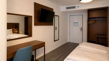 Ein Hotelzimmer mit Bett, Schreibtisch, Stuhl, Wandfernseher, Kleiderschrank und einer Tür mit Kalender.