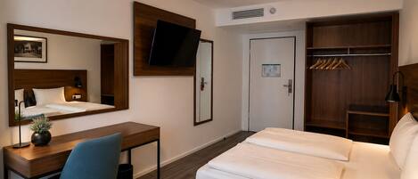 Una habitación de hotel con cama, escritorio, silla, armario y televisor fijado a la pared.