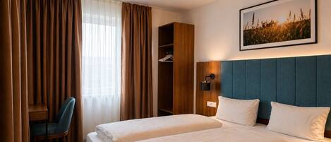 Habitación de hotel con dos camas, un escritorio, una silla, un armario y una lámpara de pared.