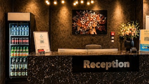 A reception desk with a marble top, a water cooler, a painting, and a sign for 'Lilly's.' - Lillys Hotel München-Unterschleißheim  (Unterschleißheim)