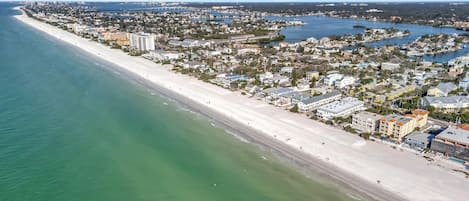 An aerial view of a coastal city with a long sandy beach, dense residential areas, and a marina.