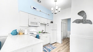 A modern kitchen with white cabinets, a microwave, a stove, and a refrigerator. There's a blue fish-shaped container on the counter. - Waterway Vista Suite Pet Friendly Boat Dock (Indian Rocks Beach)