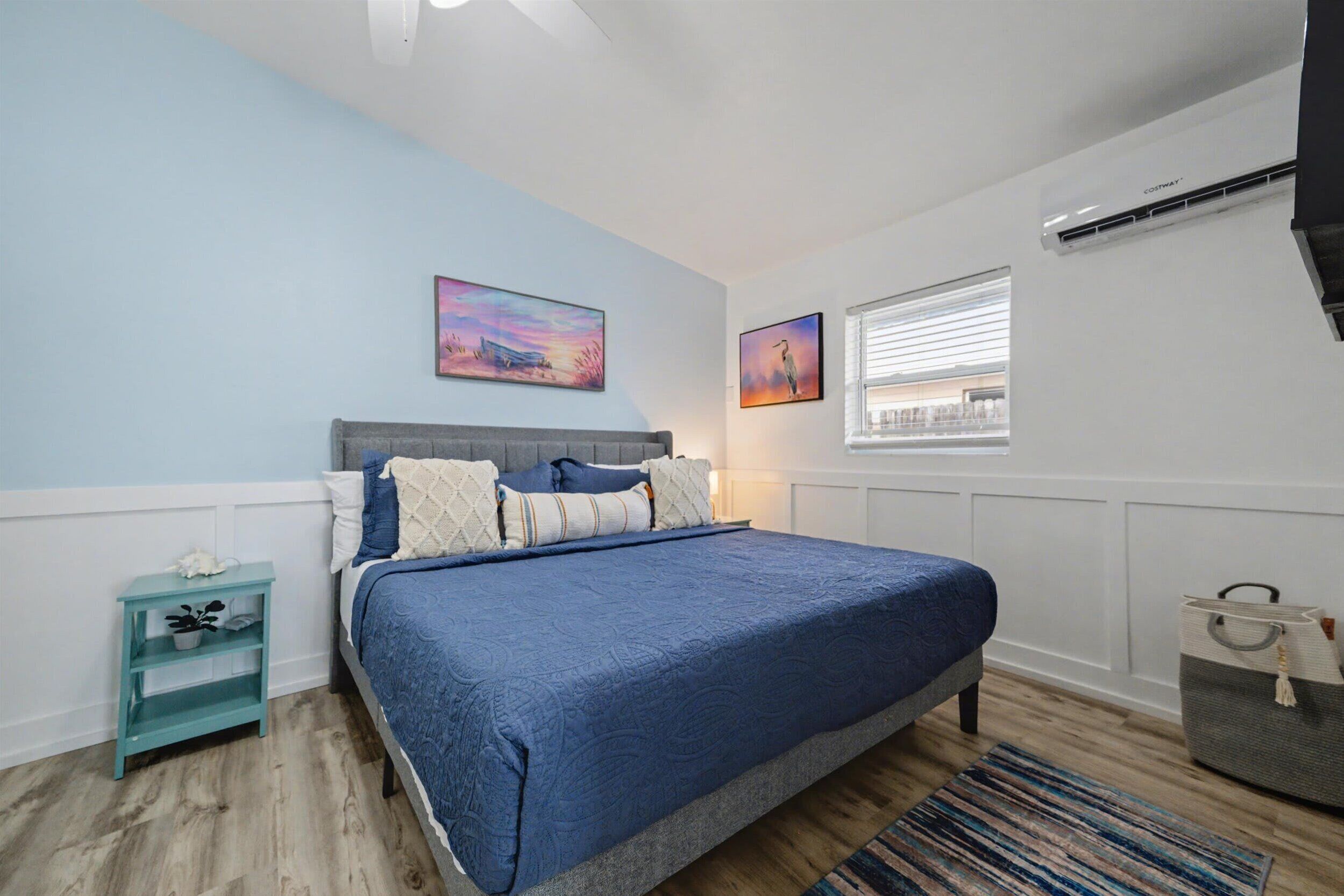 A bedroom with a bed, a nightstand, a window, and a wall-mounted air conditioner.