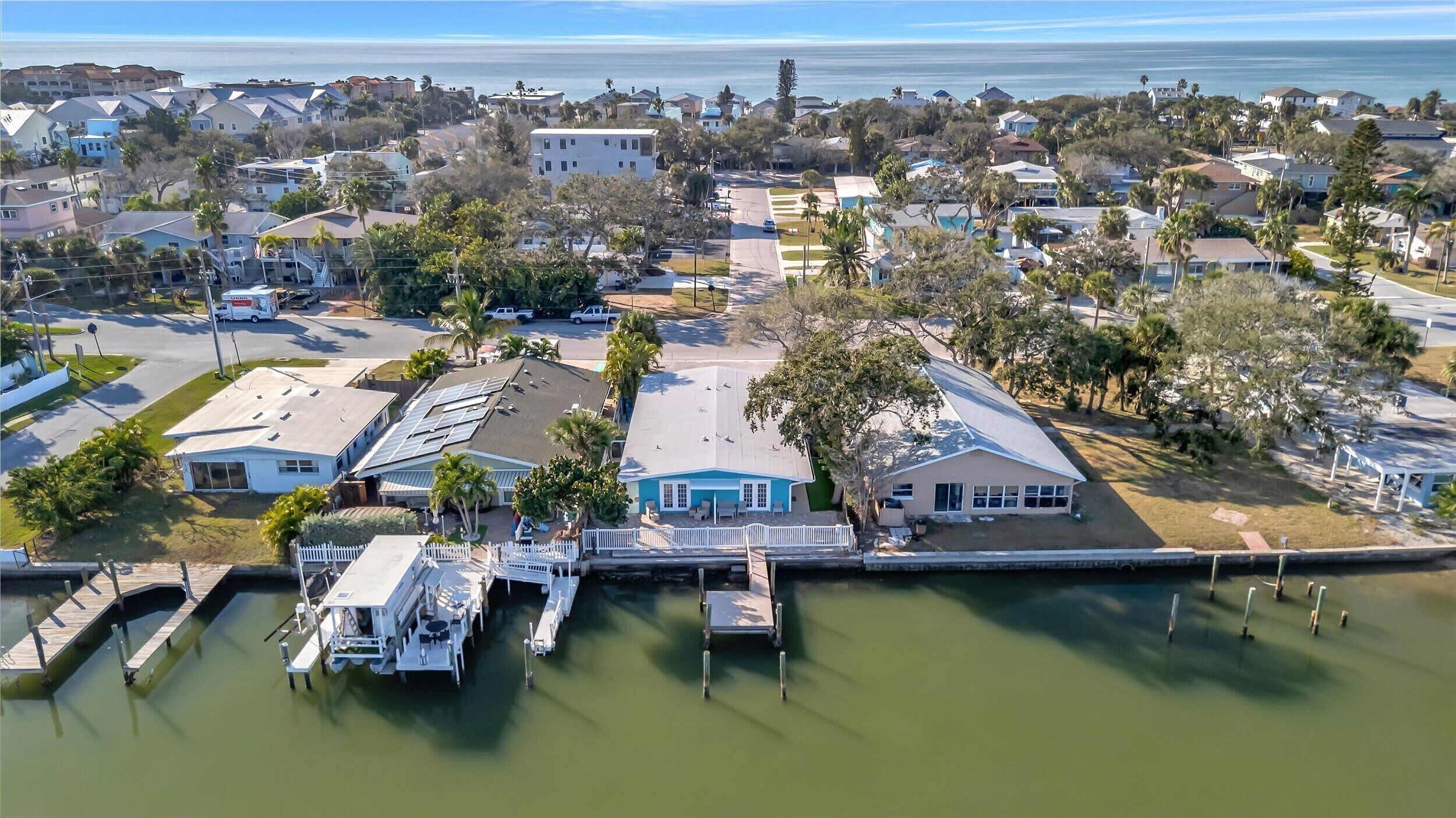 An aerial view of a coastal residential area with houses, a marina, and a clear view of the ocean.