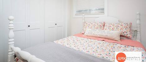 Ein Schlafzimmer mit einem Bett, einem weißen Kleiderschrank und einem Fenster mit Jalousien.
