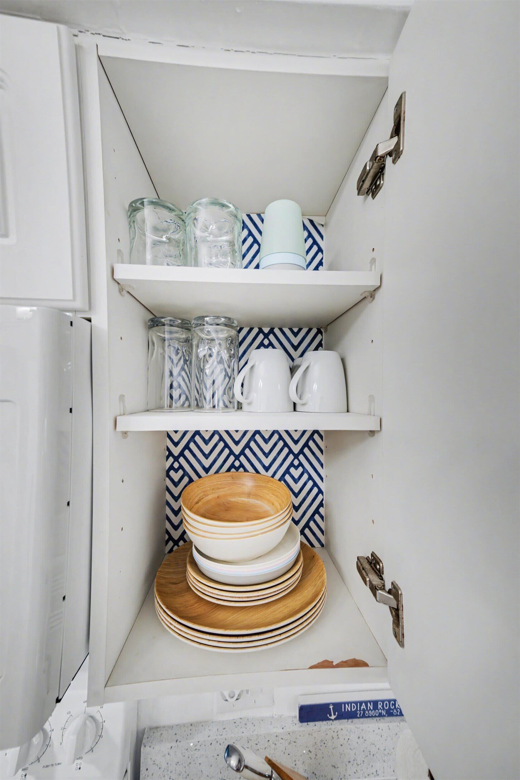 Una cocina con armarios blancos, un salpicadero estampado y estantes con frascos de vidrio, tazas y platos.