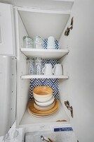 Una cocina con armarios blancos, un salpicadero estampado y estantes con frascos de vidrio, tazas y platos.