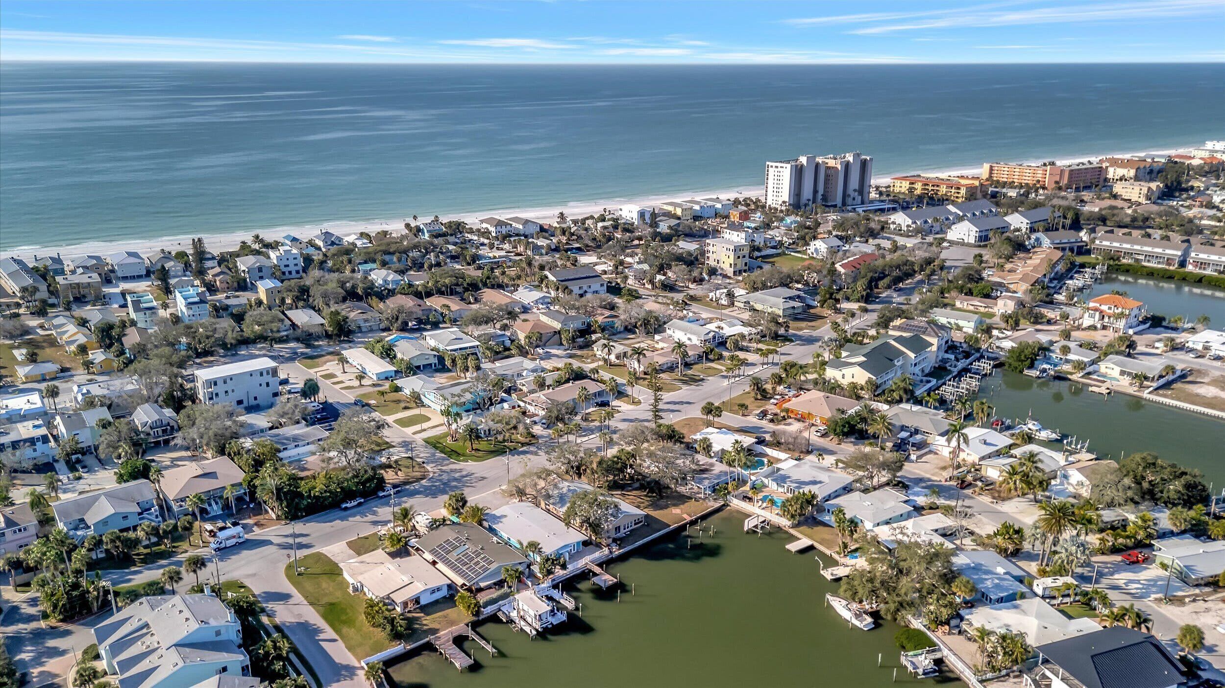 An aerial view of a coastal residential area with a marina, beachfront hotels, and a large hotel complex.