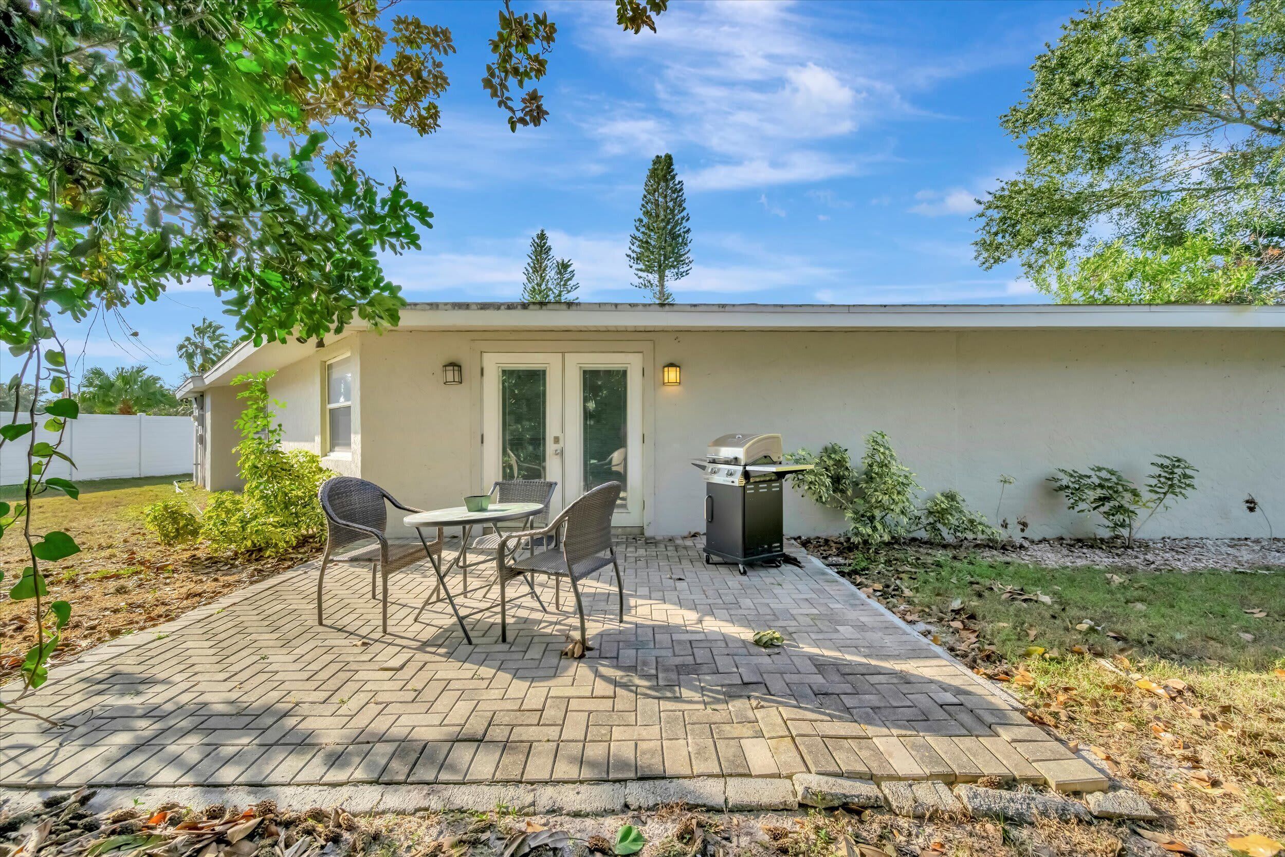 A patio with a table and chairs, a grill, and a small trash bin.