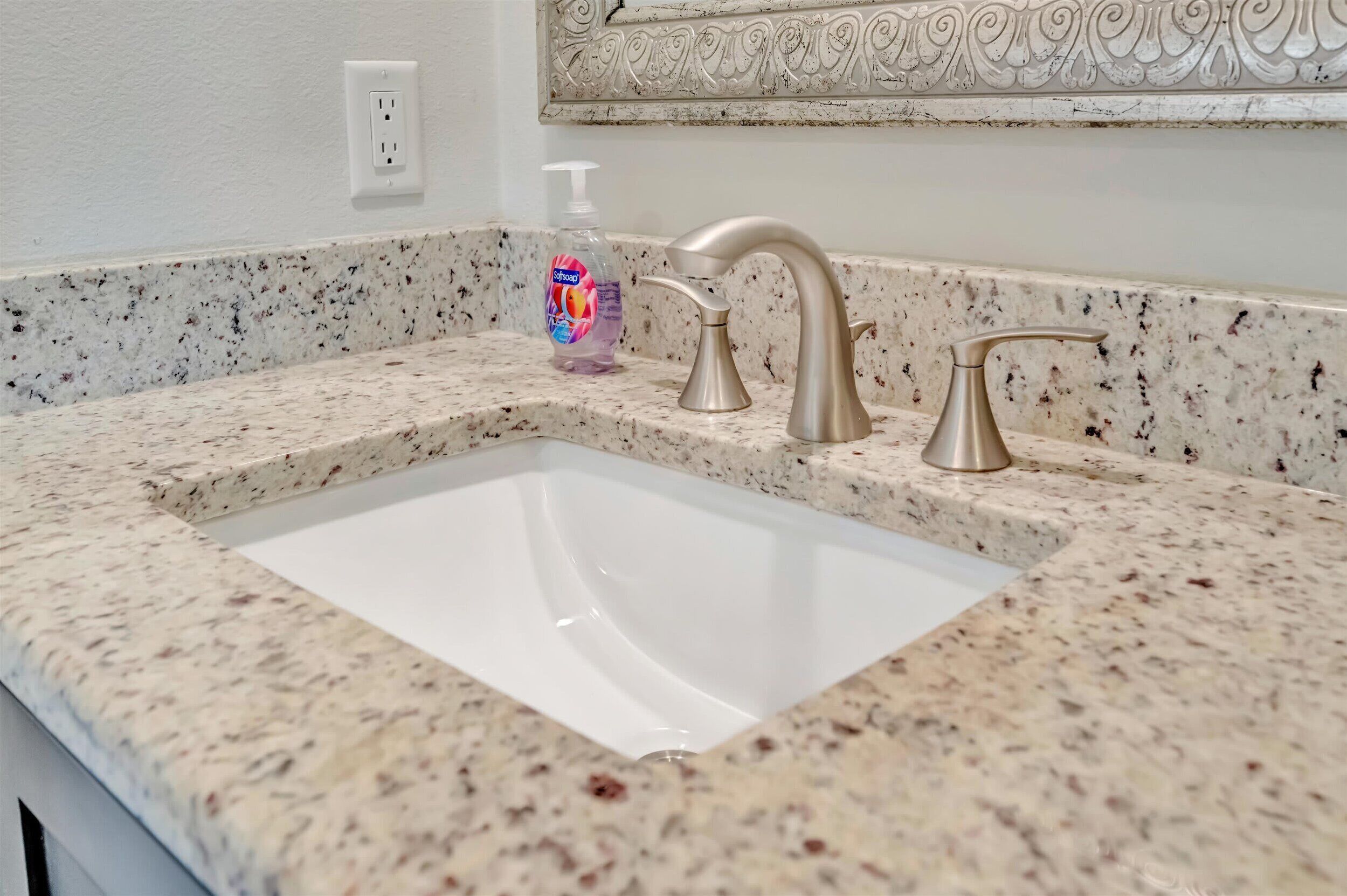 A bathroom sink with a speckled countertop, a single faucet, and a soap dispenser.