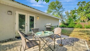 A patio with wicker chairs and a glass table, a barbecue grill, and a door with a window. - Sleeps 8 Pets Welcome Fenced In Backyard (Sarasota)