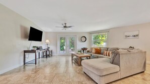 A living room with a sofa, a coffee table, a TV mounted on the wall, a ceiling fan, and a view of the outdoors through a glass door. - Sleeps 8 Pets Welcome Fenced In Backyard (Sarasota)