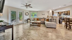 A spacious living area with a sofa, coffee table, and dining table. There is a ceiling fan, a kitchen in the background, and large windows. - Sleeps 8 Pets Welcome Fenced In Backyard (Sarasota)