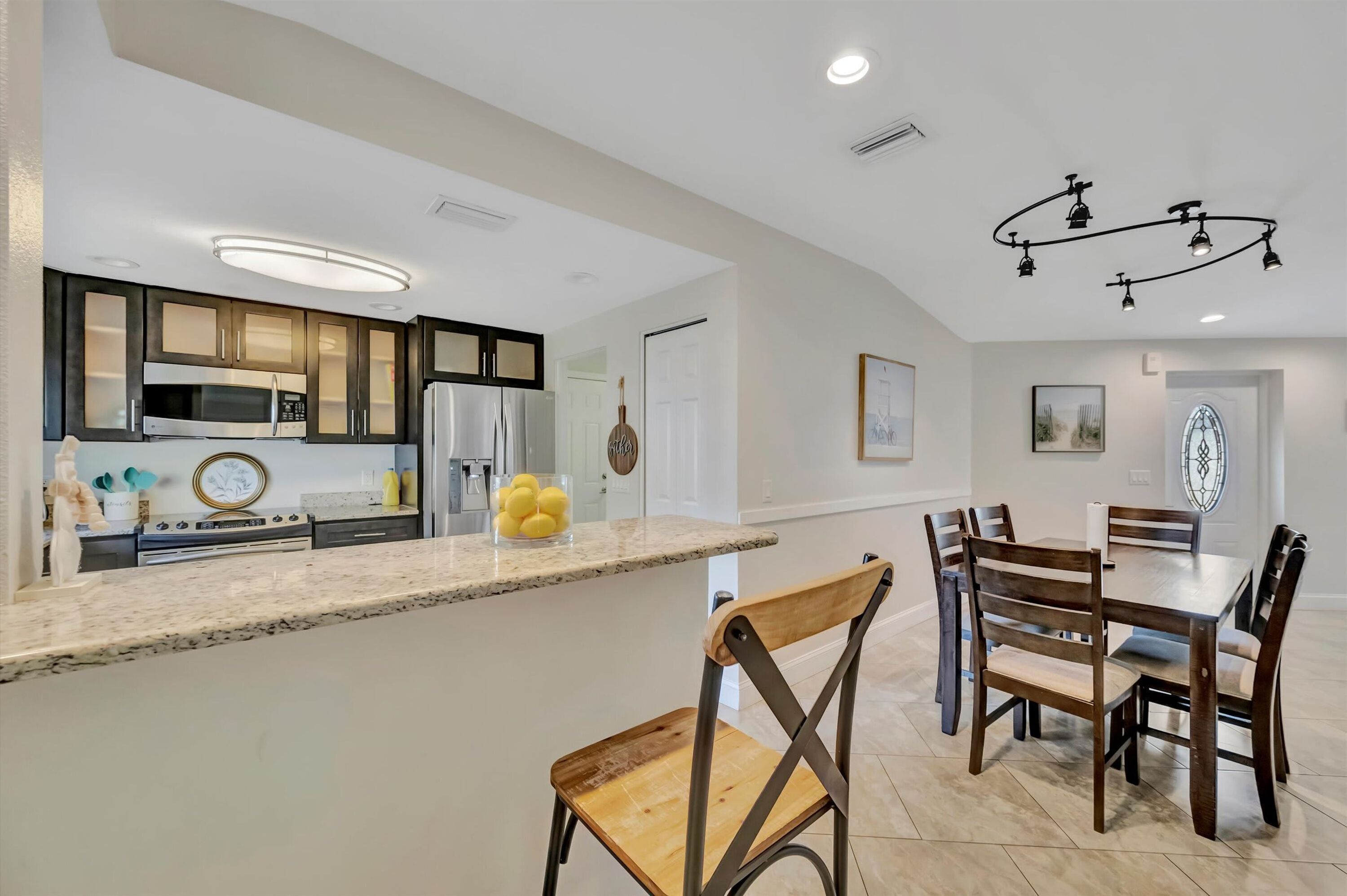 A modern kitchen with built-in appliances, a dining area with wooden chairs, and a ceiling light fixture.