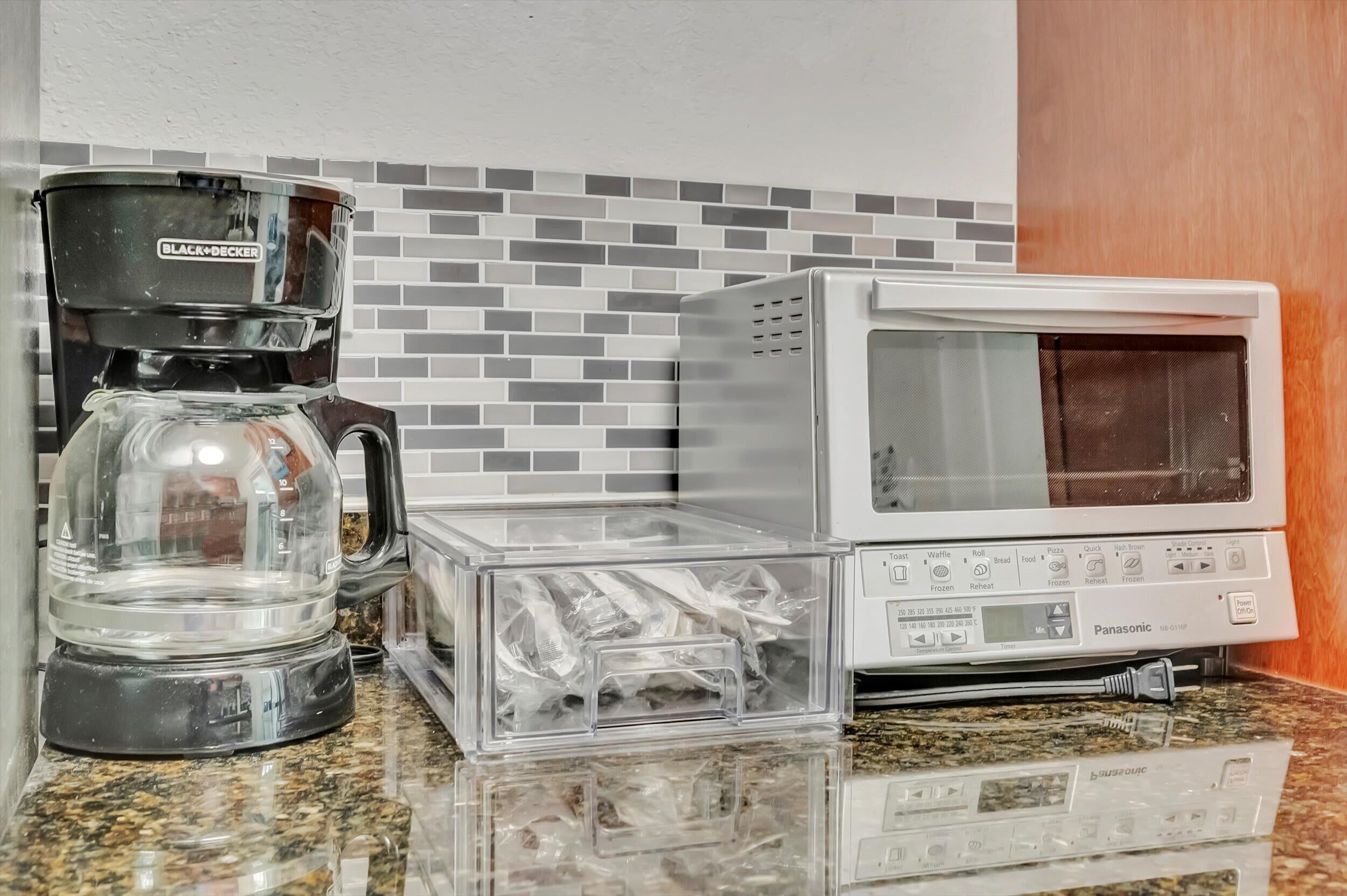 Una cocina con cafetera, microondas y recipientes de plástico en la encimera.