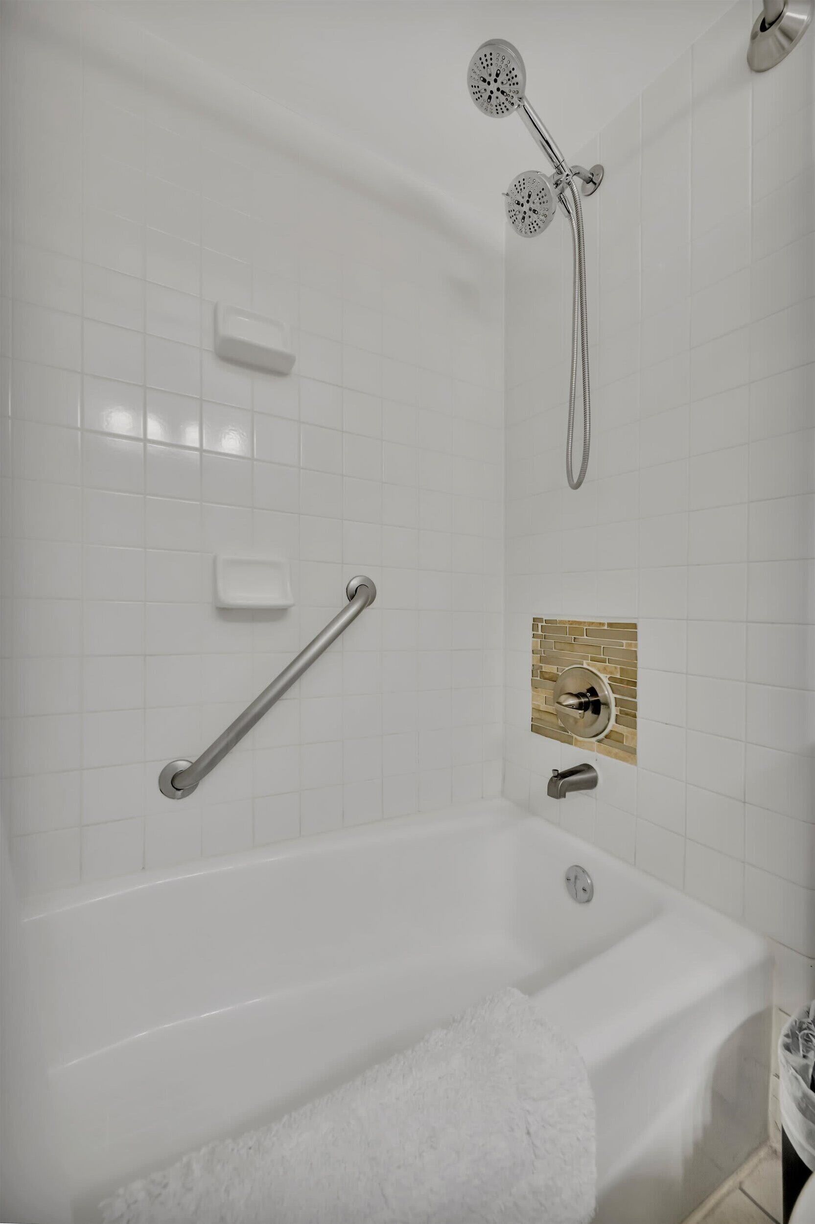 A modern bathroom with a bathtub, a handheld showerhead, a handheld showerhead, a towel rack, and a soap dish.