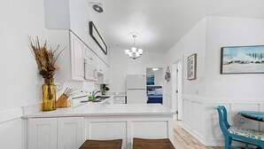 A kitchen with white cabinetry, a central island with stools, a chandelier, and a painting of a beach scene. - Walk to the Beach Pets OK Waterfront King Bed (Indian Rocks Beach)