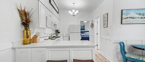 A kitchen with white cabinetry, a central island with stools, a chandelier, and a painting of a beach scene.