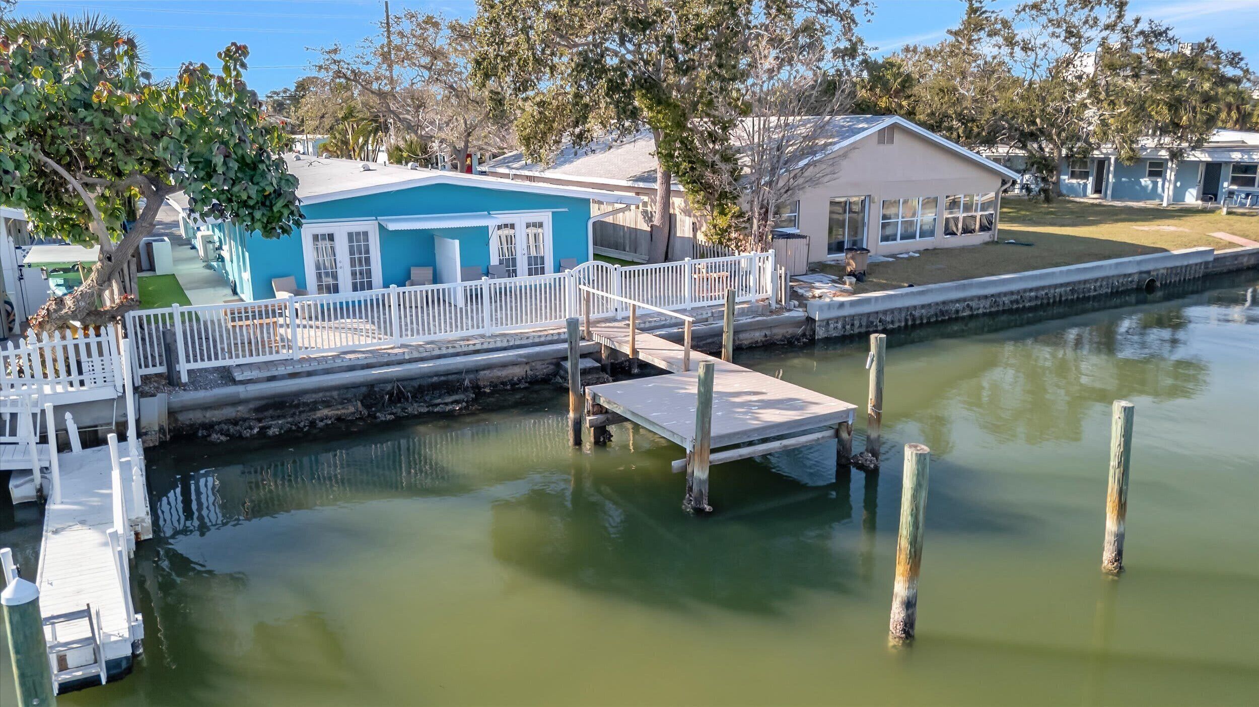 A waterfront property with a dock, a small building with a blue exterior, and a grassy area.