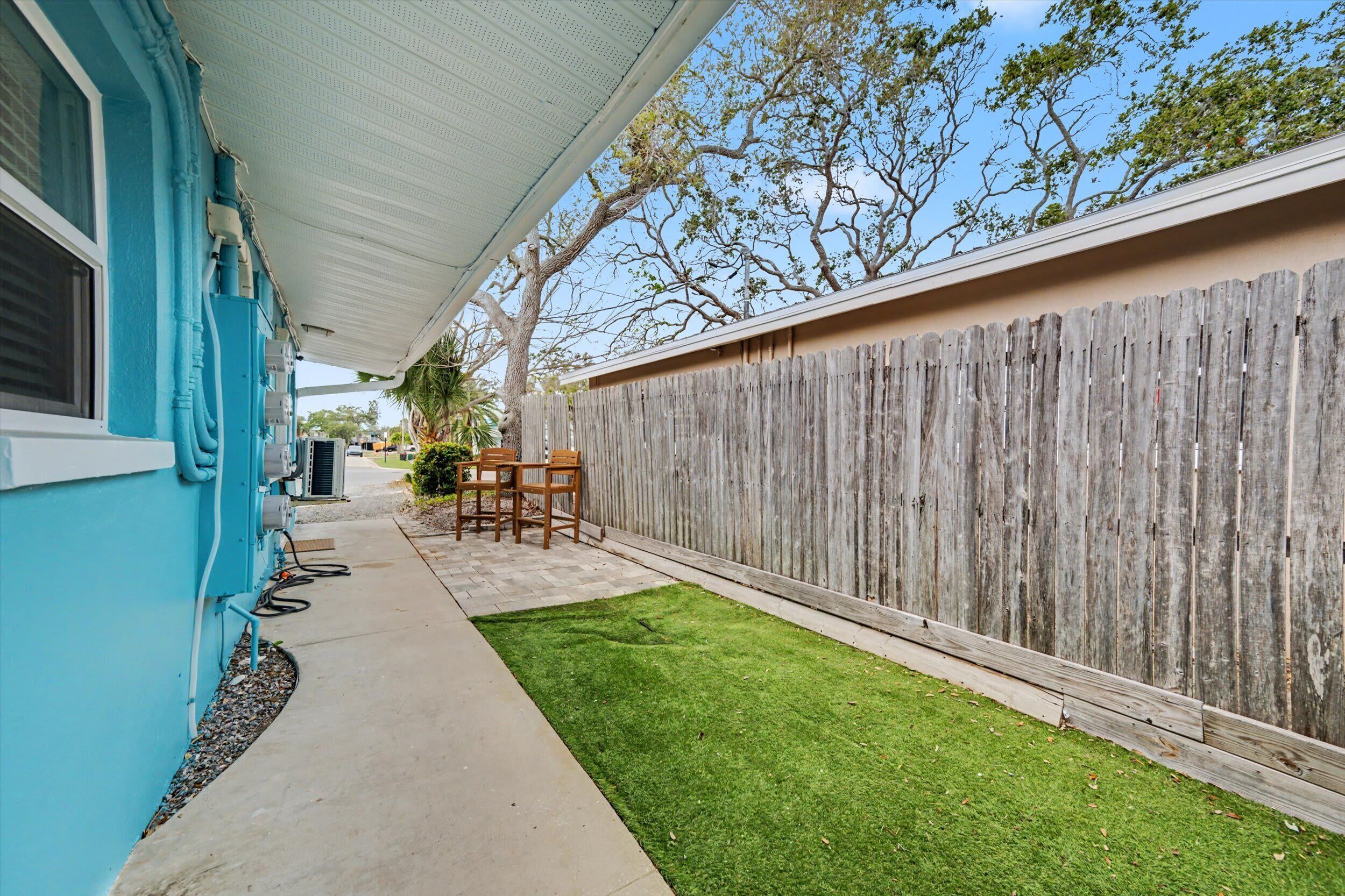 A backyard with a wooden fence, a blue house, and a small lawn.