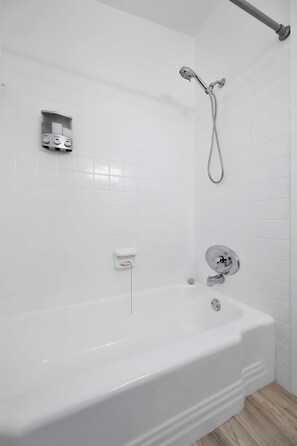 Un baño moderno con una bañera blanca, un cabezal de ducha manual y un dispensador de jabón en la pared.