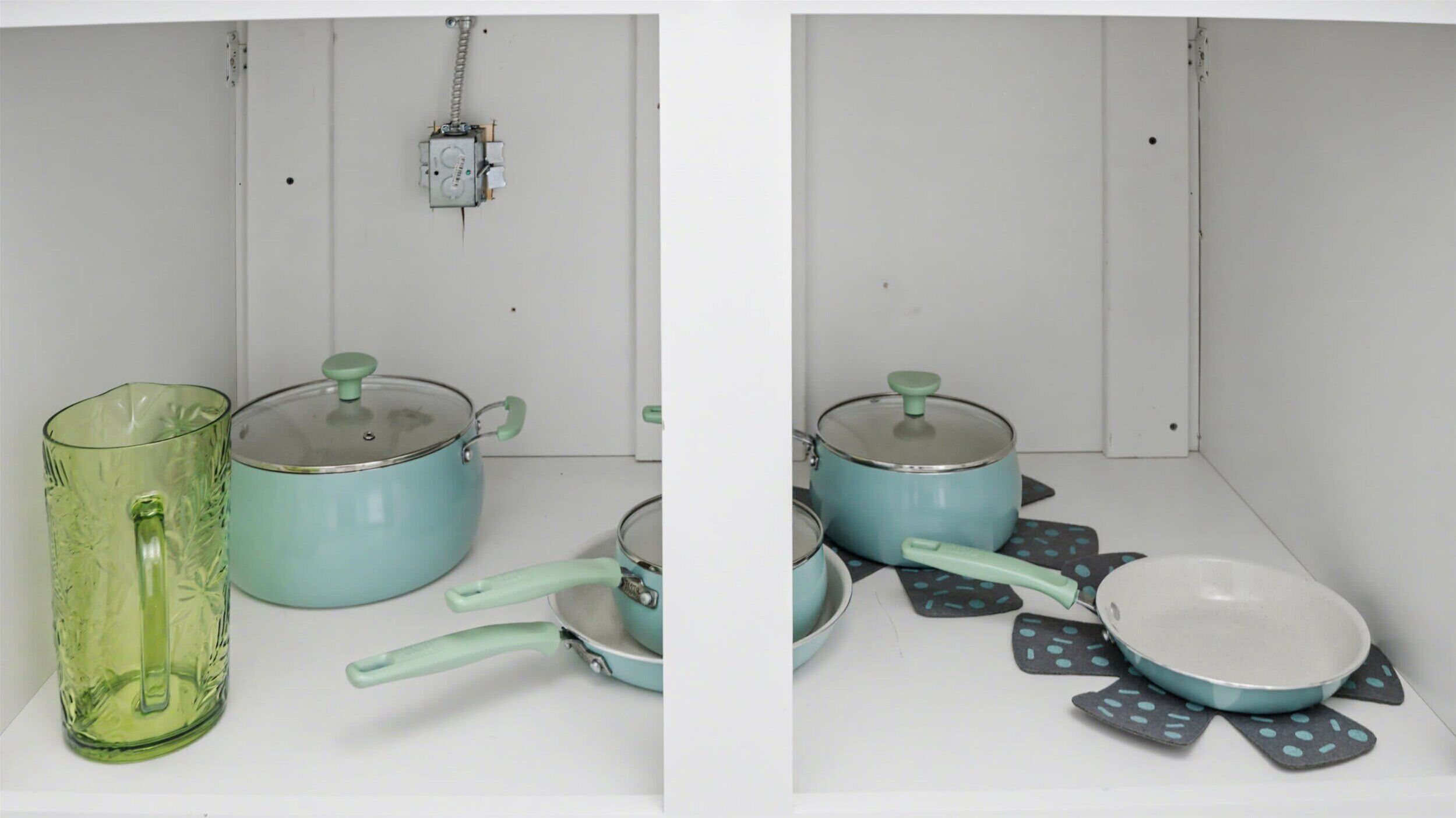 A kitchen with a white countertop, a green glass pitcher, a blue pot with a lid, a blue pan, and a blue bowl with a lid.