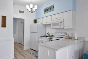 Una cocina moderna con armarios blancos, microondas, estufa y fregadero. Hay un letrero de madera en la pared y una planta en la encimera.