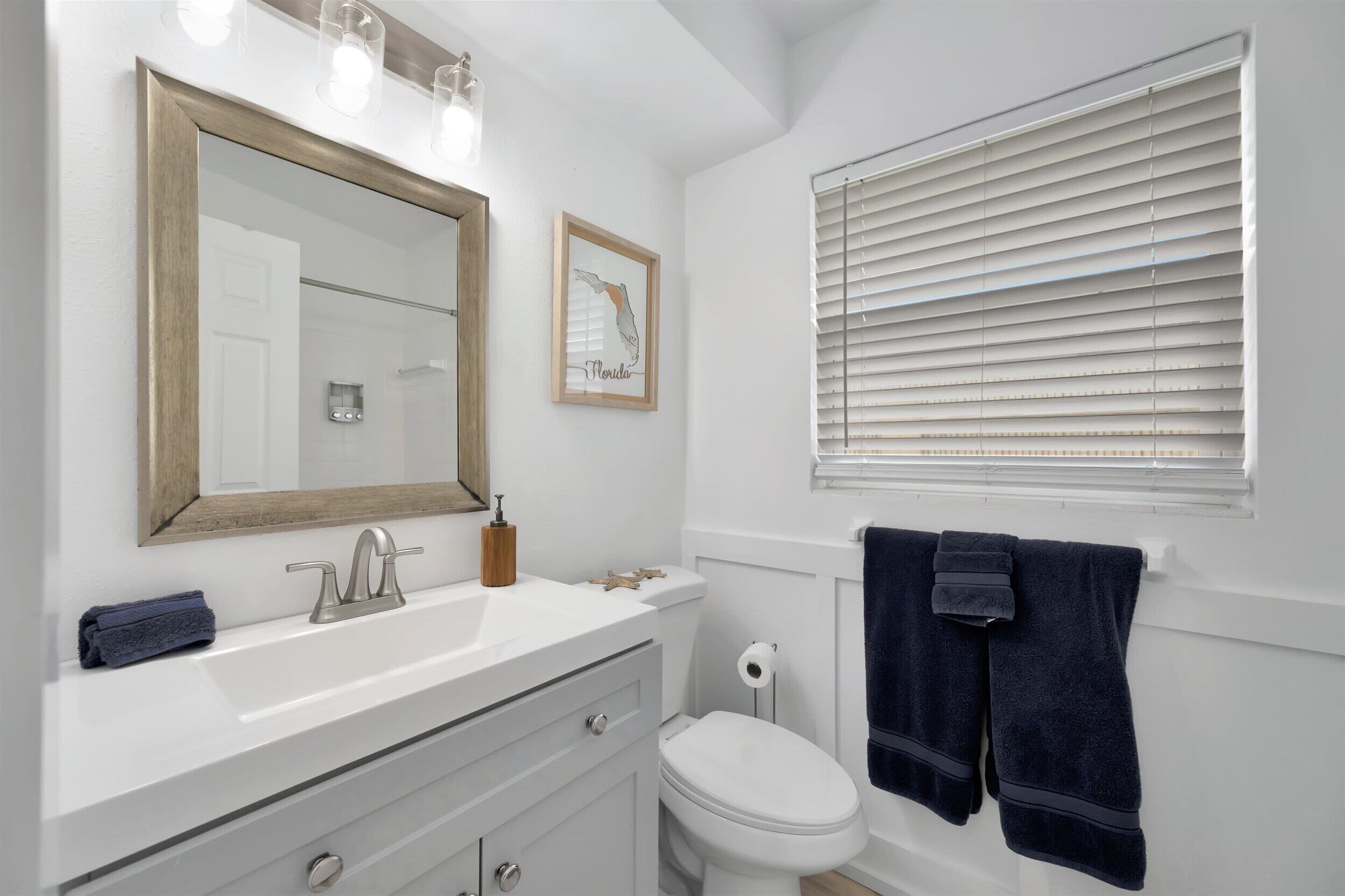 Un bagno con un mobile lavabo bianco, uno specchio grande, un water e una finestra con persiane.
