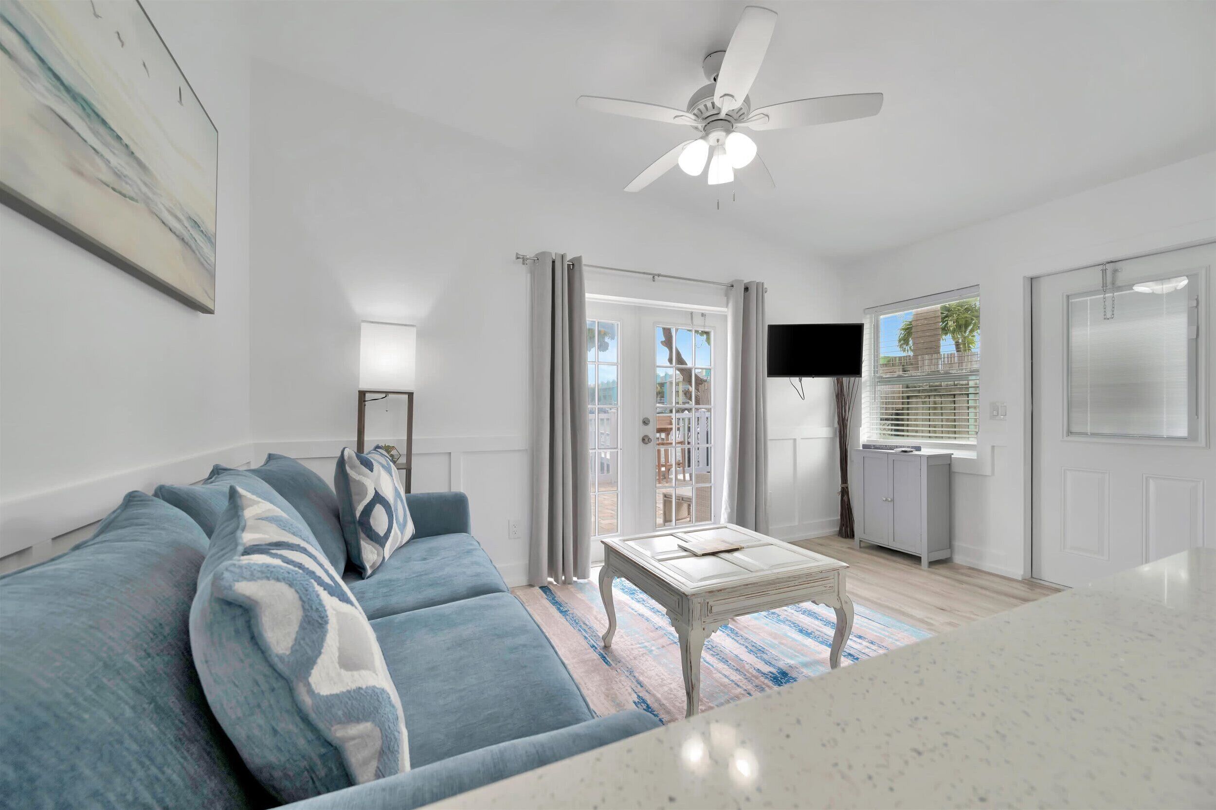 A modern living room with a blue sofa, a white coffee table, and a ceiling fan.