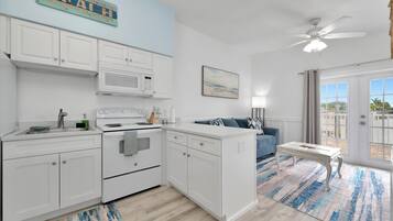 A modern kitchen with white cabinets, a microwave, and an oven. There's a blue couch and a small table in the living area.