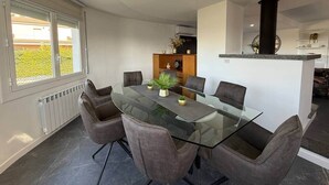 A modern dining area with a glass table surrounded by six chairs, a central plant, and a kitchen island with a black chimney. - Villa Vora a mar in Calafell (Calafell)