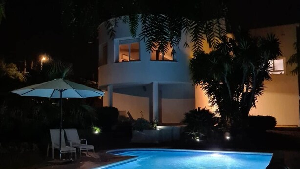 A nighttime swimming pool area with a two-story building in the background, surrounded by trees and a few lounge chairs. - Villa Vora a mar in Calafell (Calafell)