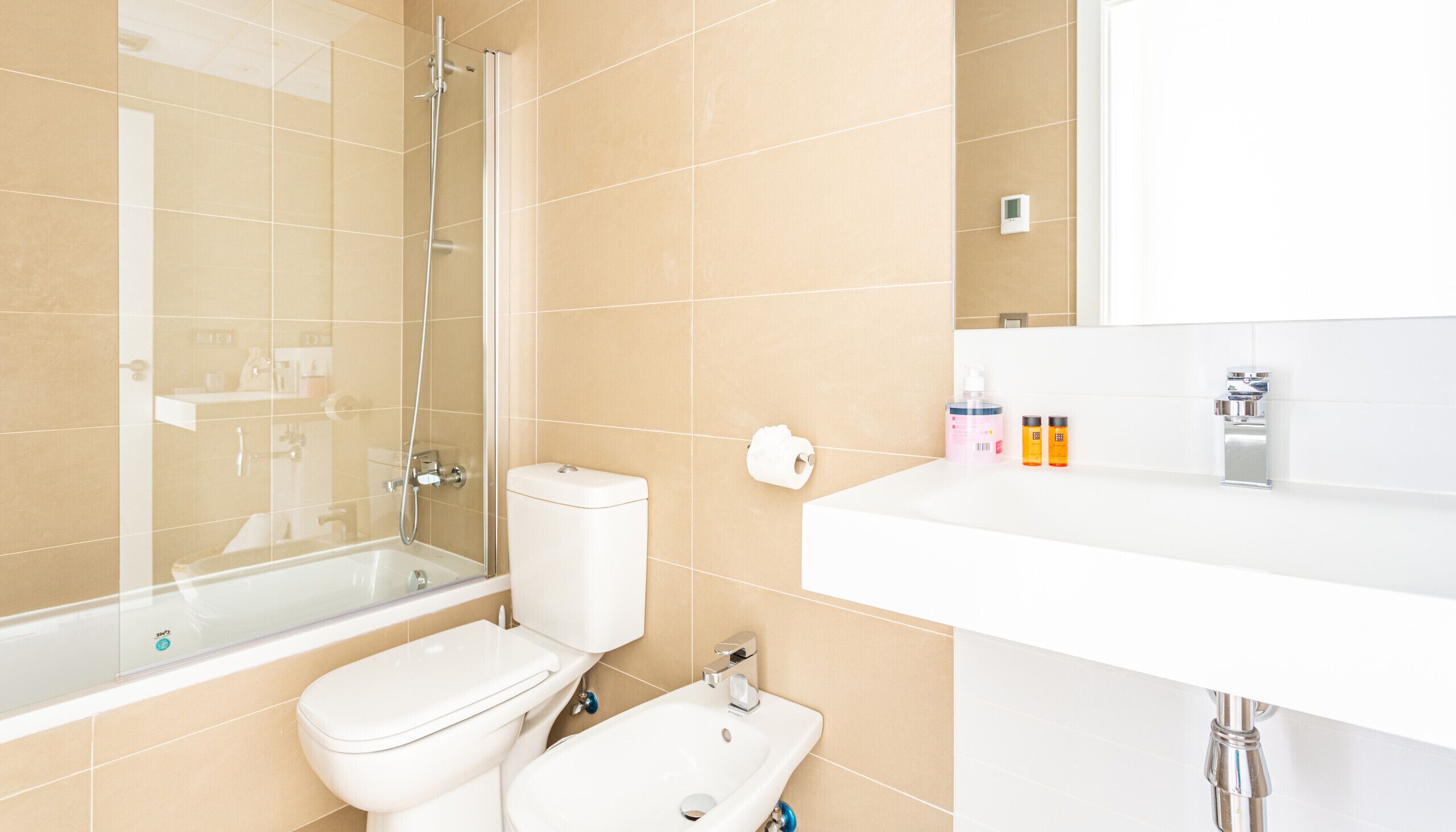 Une salle de bain moderne avec une douche à parois de verre, des toilettes, un bidet et un lavabo équipé de produits de toilette.