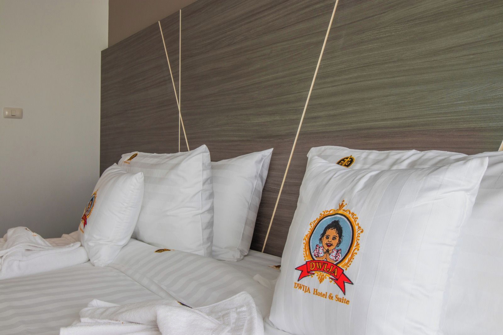 A hotel room with a bed featuring white bedding and pillows with a logo and text.
