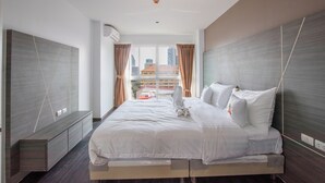 Una habitación de hotel moderna con una cama grande, almacenamiento integrado, vistas a la ciudad y un equipo de aire acondicionado instalado en el techo.