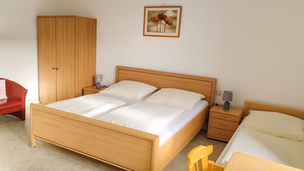 Un dormitorio con una cama de madera, mesitas de noche, un armario, una silla y un escritorio.