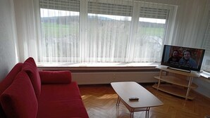 A living room with a red sofa, a small white table, and a TV on a stand. - Hotel Kremer  (Buechenbeuren)