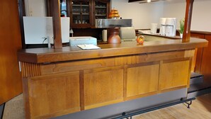 A wooden reception desk with a printer, a glass cabinet with glassware, and a coffee machine. - Hotel Kremer  (Buechenbeuren)