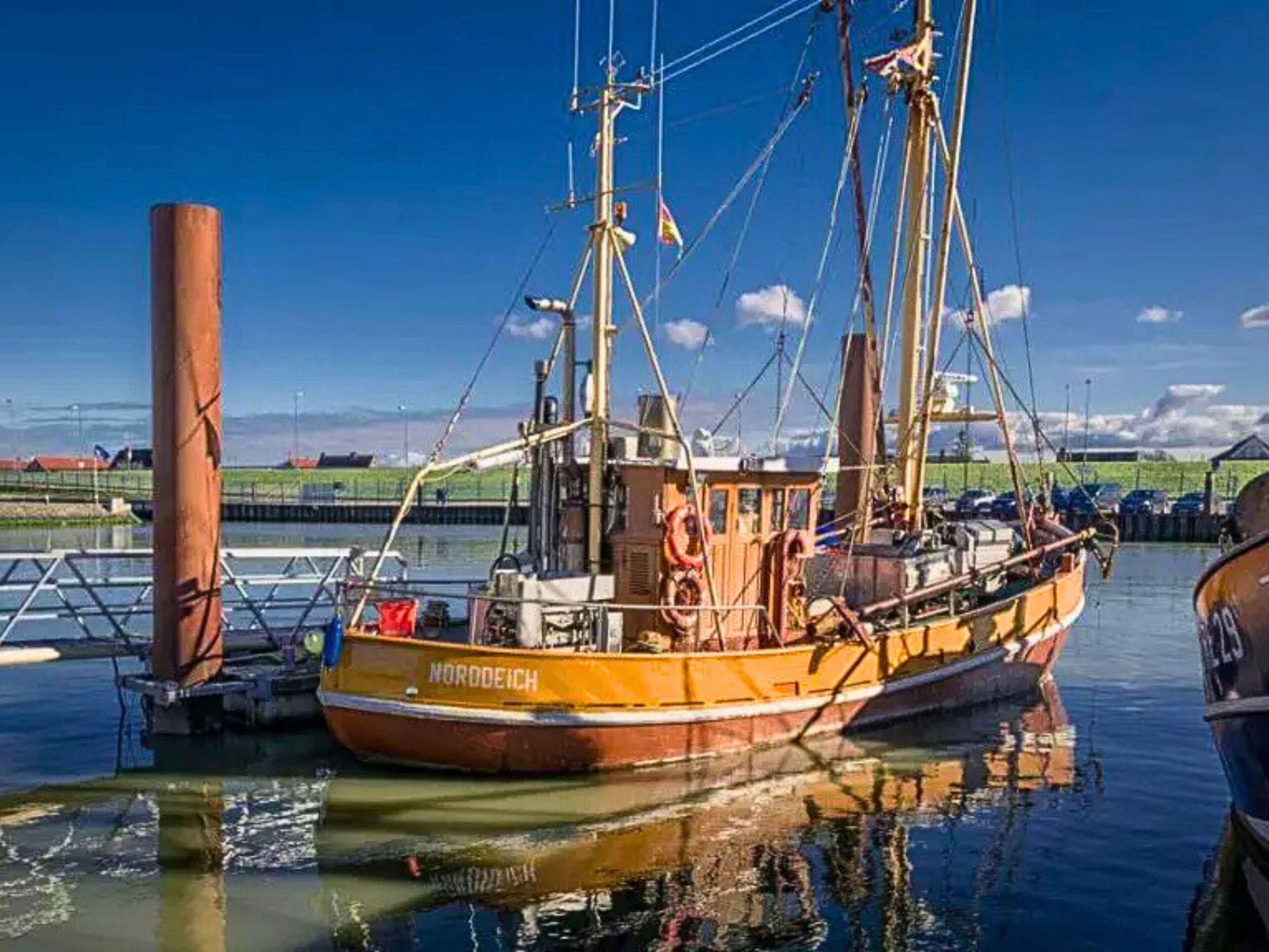 Een grote oranje boot aanmeren bij een steiger, met een heldere lucht en rustig water.