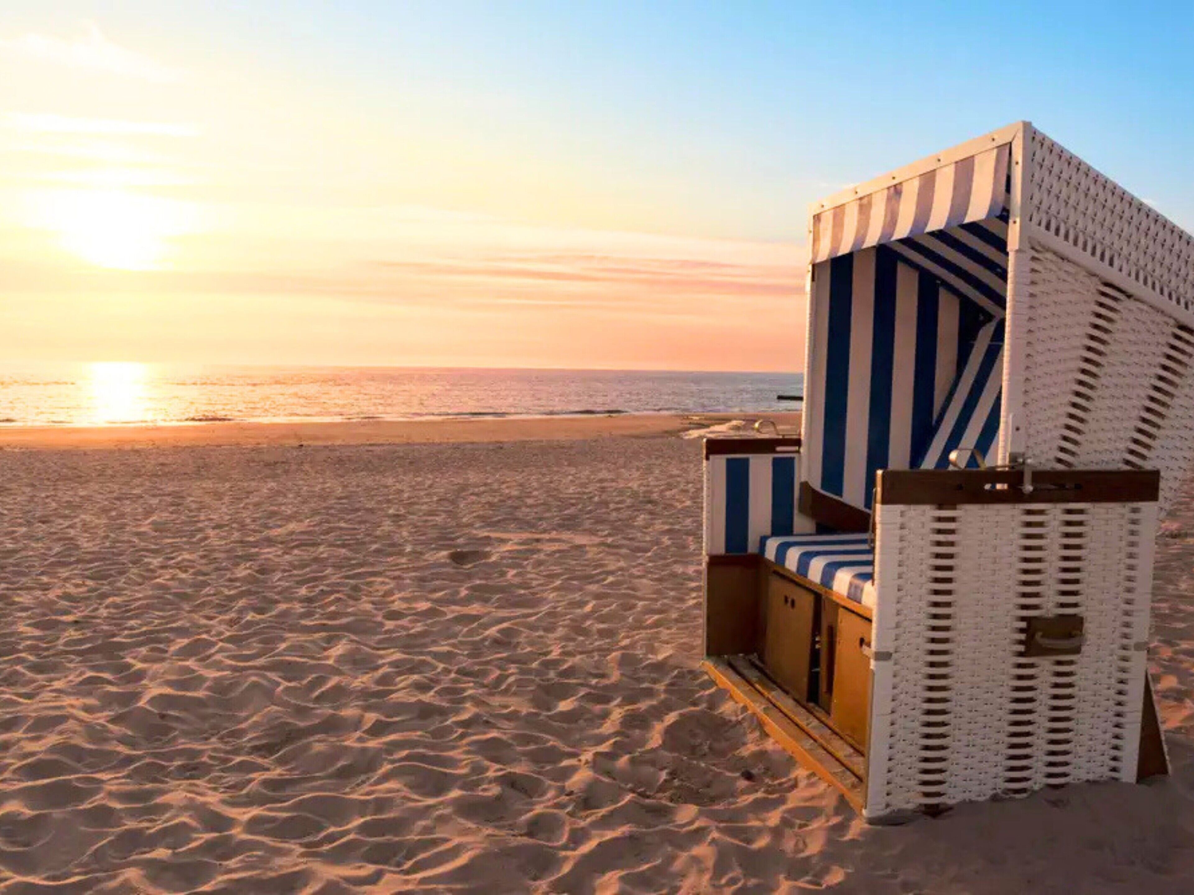 Ein Liegestuhl mit gestreifter Auflage, platziert an einem Sandstrand mit Sonnenuntergang im Hintergrund.