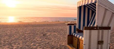Ein Liegestuhl mit gestreifter Auflage, platziert an einem Sandstrand mit Sonnenuntergang im Hintergrund.