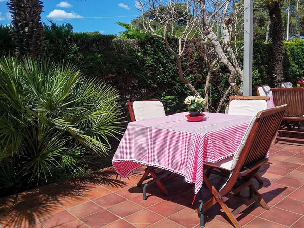 Una terrazza esterna con tovaglia a scacchi, sedie di legno e una pianta in vaso.