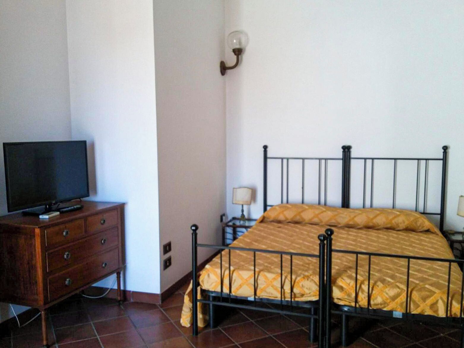A bedroom with a bed, a dresser, a television, and a wall-mounted light fixture.