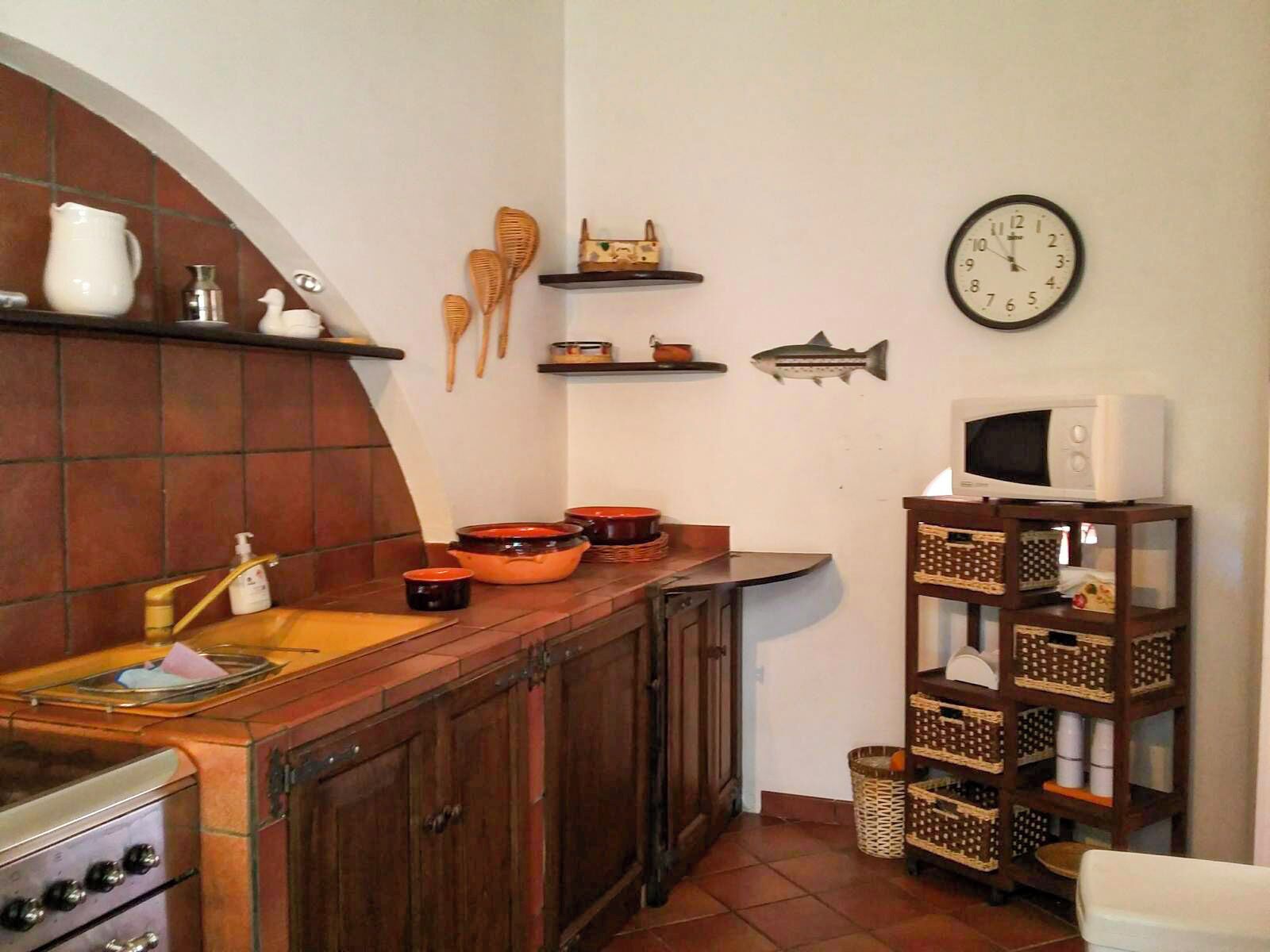 Une cuisine avec des meubles de rangement en bois, une cuisinière, un four à micro-ondes, ainsi que divers ustensiles et de la vaisselle rangés sur des étagères.
