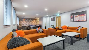 A modern lounge area with orange sofas, a pool table, and a brick accent wall. - Student Only Mary Parker House (Plymouth)