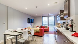 A modern kitchen with a dining area, a red sofa, and a TV mounted on the wall. - Student Only Mary Parker House (Plymouth)