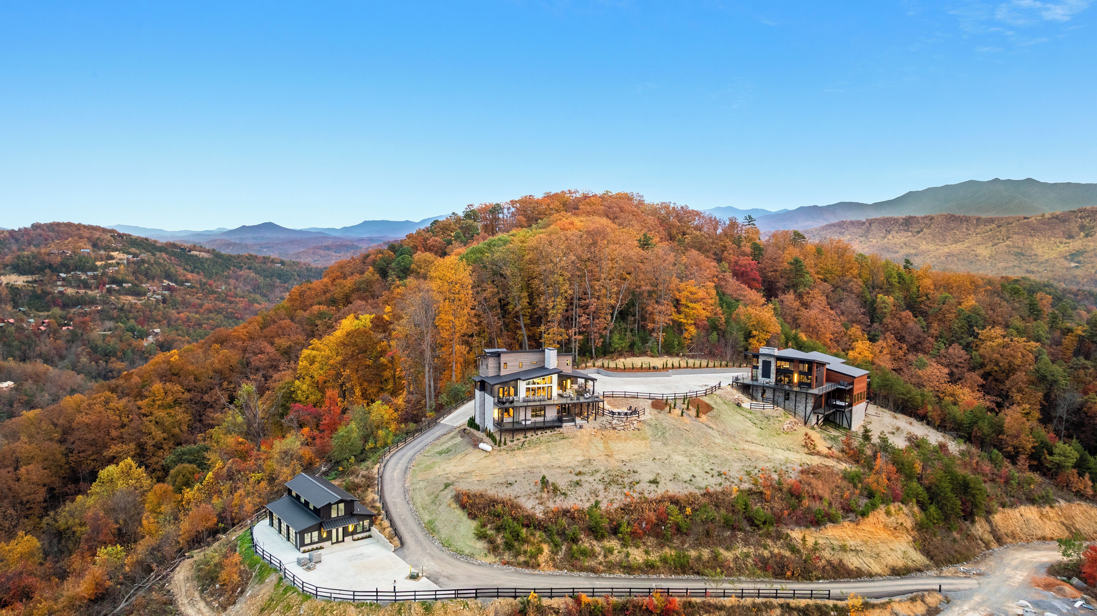 A modern two-story house with a large deck, surrounded by a forested hillside.