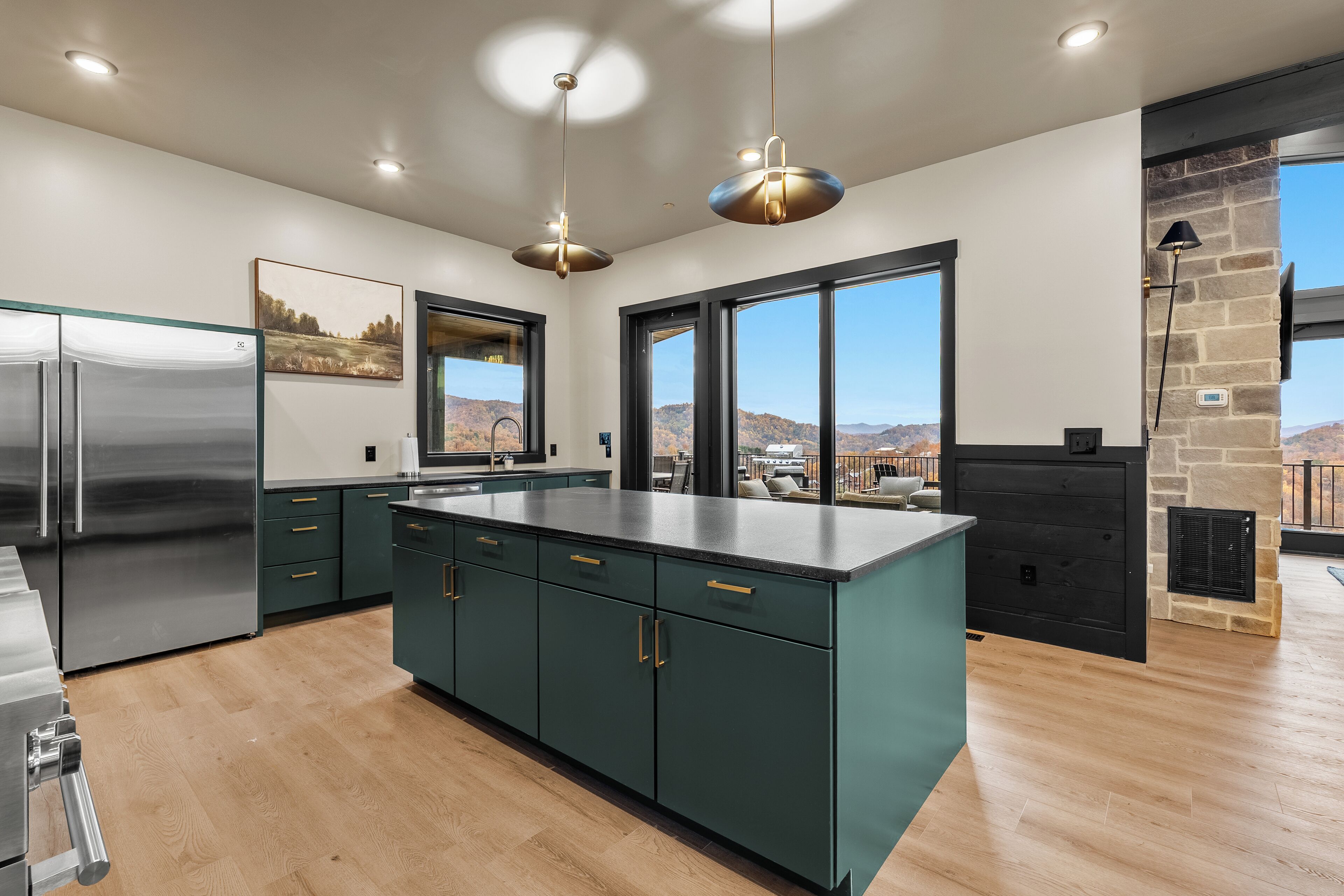 Une cuisine moderne dotée d’un grand îlot central, d’appareils électroménagers en acier inoxydable, de meubles de couleur turquoise et de grandes fenêtres offrant une vue sur les montagnes.