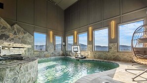 Une piscine intérieure aux murs en pierre, dotée de grandes fenêtres et d’une cheminée en pierre.